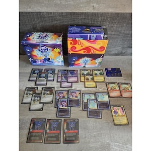 May include: Two boxes of My Little Pony trading cards with various cards scattered in front. The boxes are blue and purple with images of ponies. The cards feature colorful illustrations of the ponies and other characters from the show.