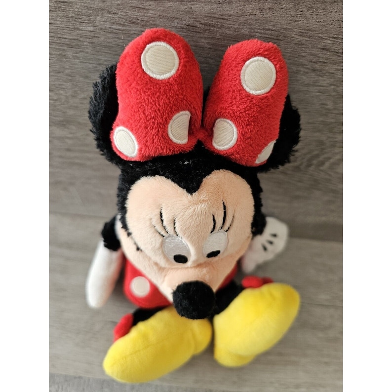 K&ouml;nnte beinhalten: Ein Pl&uuml;schtier von Minnie Maus, mit einer roten Schleife mit wei&szlig;en Punkten, schwarzen Ohren, einer schwarzen Nase und gelben Schuhen.