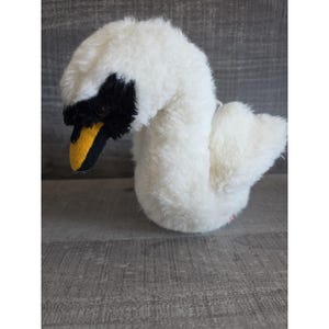 May include: A plush swan toy with white, fluffy feathers. The swan has a black head and a yellow beak. The toy is designed to resemble a swan and is made of soft, plush material.