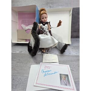 May include: A Madame Alexander doll from The Fashion Collection Platinum series. The doll is dressed in a white satin dress with a black and brown floral design, brown gloves, and a fur stole. The doll is in its original box with a welcome card.
