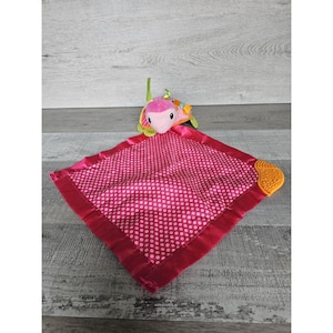 May include: Pink and white polka dot baby blanket with a pink and green turtle plush toy attached. The turtle has a textured orange foot.