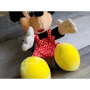 Pu&ograve; includere: Un giocattolo di peluche di Topolino vestito con un vestito a pois rossi e bianchi. Il giocattolo ha orecchie nere, un naso nero e piedi gialli.