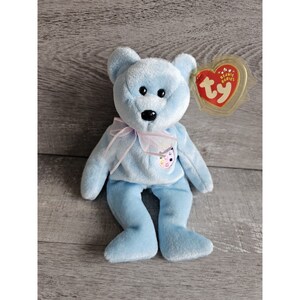 May include: A light blue beanie baby bear with a pink ribbon around its neck and a colourful heart-shaped tag that says "ty beanie babies".