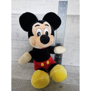 May include: A black and red plush Mickey Mouse toy with yellow shoes. The toy is sitting on a wooden surface.