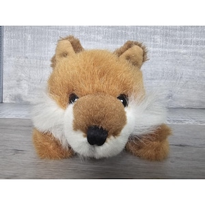 May include: A plush fox toy with a brown and white fur pattern. The fox has a black nose and brown eyes.
