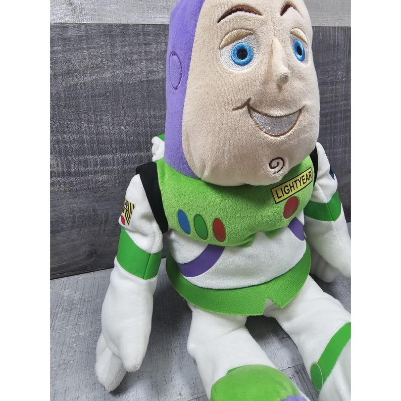 May include: A plush Buzz Lightyear doll, with a purple and white helmet, green and white spacesuit, and the name "LIGHTYEAR" on the chest. The doll has a smiling face with blue eyes and is made of soft, plush material.