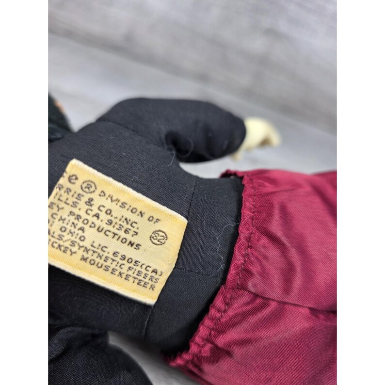 May include: A vintage Mickey Mouse plush doll, featuring a black jacket, burgundy pants, and cream-colored hands. The doll has a tag that reads "Harris & Co., Inc." and "Mickey Mouseketeer."