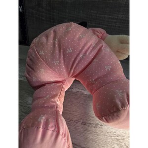 Puede incluir: Una mu&ntilde;eca de peluche rosa con un lazo blanco y un estampado de lunares. El cuerpo de la mu&ntilde;eca est&aacute; hecho de tela suave y tiene una forma redondeada. Los brazos y las piernas de la mu&ntilde;eca son visibles, y el dise&ntilde;o general es simple y lindo.