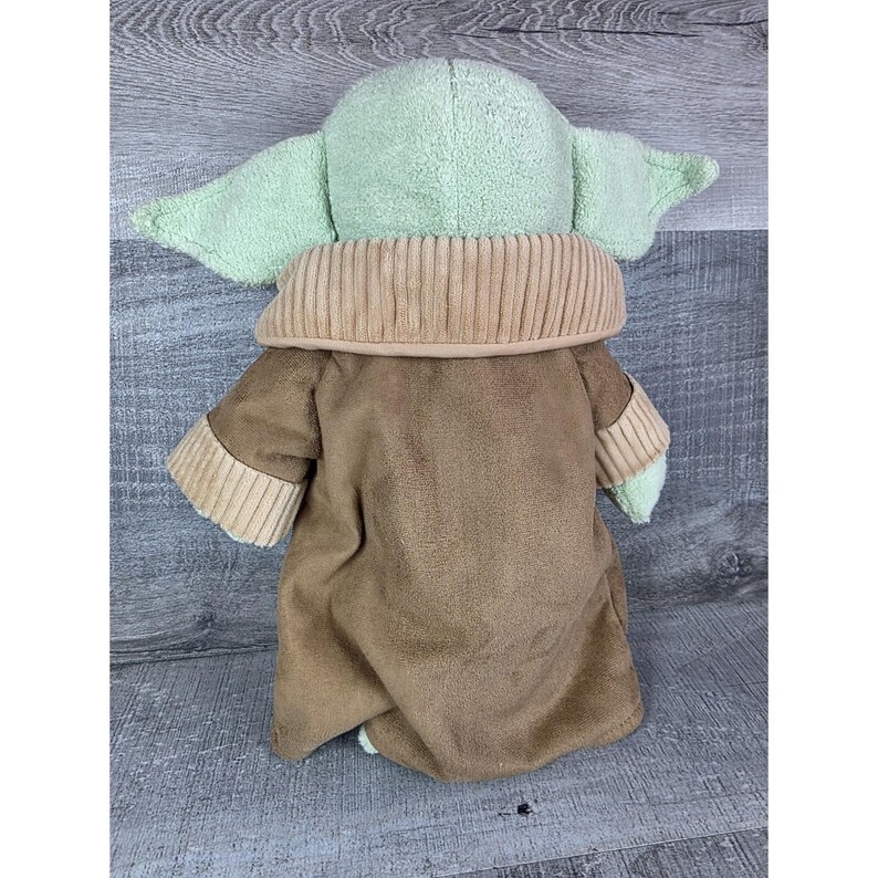 May include: A plush doll of a character with large ears and a tan coat. The doll has a light green head and ears, a tan collar, and a brown coat. The doll is made of soft, plush material.