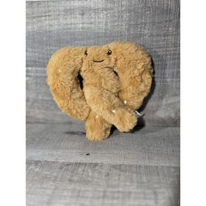 May include: A plush pretzel toy with a smiling face and rosy cheeks. The soft, brown pretzel has a classic twisted shape and white speckles. This cuddly toy is perfect for children and pretzel lovers.