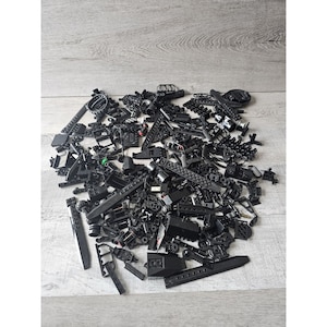 Puede incluir: Un montón grande de piezas de Lego negras, incluyendo varias formas, tamaños y texturas. Las piezas están esparcidas sobre una superficie de madera clara.