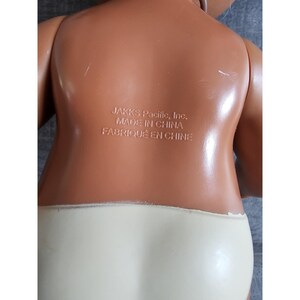 Pu&ograve; includere: Una bambola di plastica marrone con un pannolino bianco. La bambola ha un'etichetta sul retro che recita "JAKKS Pacific, Inc. MADE IN CHINA FABRIQU&Eacute; EN CHINE".