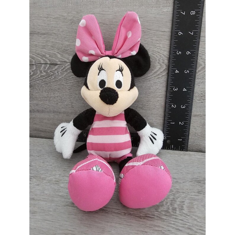May include: A pink and black plush toy of Minnie Mouse wearing a pink and white polka dot bow and a pink and white striped swimsuit.
