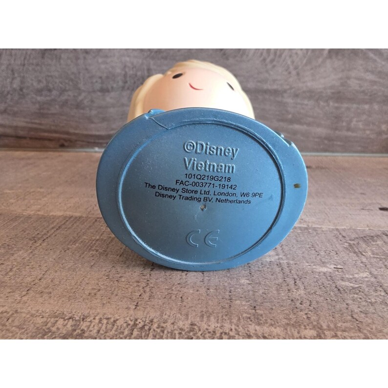 May include: A light-colored figurine with a blue base, featuring the text "Disney Vietnam." The figurine has a smiling face and blonde hair. The base includes the text "The Disney Store Ltd, London, W6 9PE" and "CE."