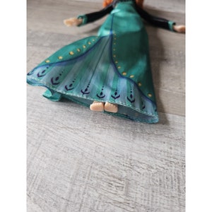 May include: A green and blue dress with gold accents and a pattern of stylized leaves. The dress is made of a soft, silky fabric and has a flowing skirt.