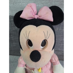 Puede incluir: Mu&ntilde;eca de peluche de Minnie Mouse con un lazo rosa, orejas negras y un vestido rosa. La mu&ntilde;eca tiene ojos grandes y redondos y largas pesta&ntilde;as. Un biber&oacute;n est&aacute; sujeto a la mano de la mu&ntilde;eca. Un juguete cl&aacute;sico para ni&ntilde;os.