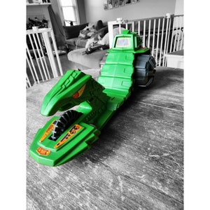 May include: A green toy vehicle with a long, segmented track and a bird-like head. The vehicle has orange and black details and the text "665" on the side.