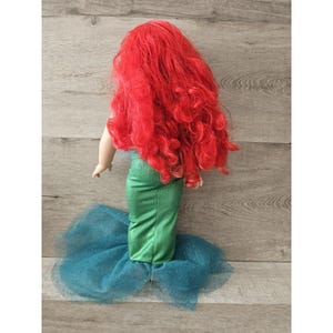 Puede incluir: Una mu&ntilde;eca con el pelo rojo que lleva una cola de sirena verde con una falda de tul azul.