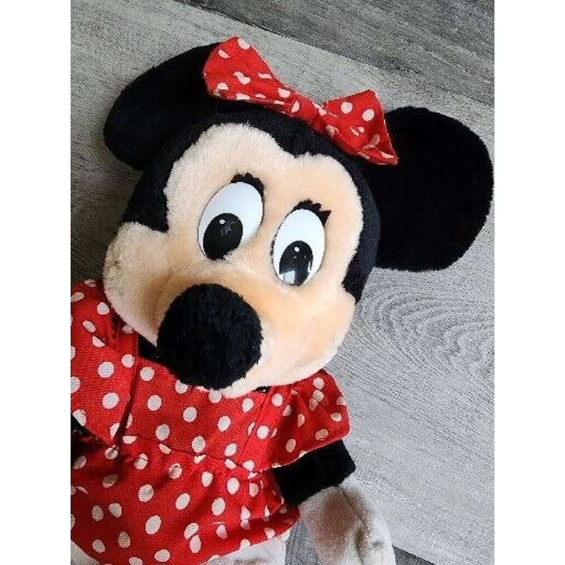 Peut inclure: Un jouet en peluche de Minnie Mouse, la petite amie de Mickey Mouse. Elle porte une robe rouge &agrave; pois blancs et un n&oelig;ud rouge dans les cheveux.
