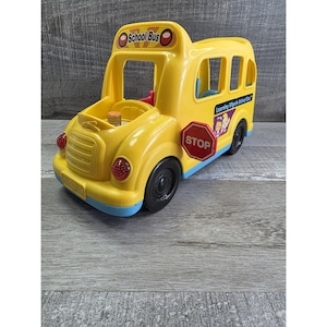 May include: A yellow toy school bus with black wheels, red stop sign, and the words "School Bus" on top. The bus has a blue trim and the words "Learning Wheels School Bus" on the side.