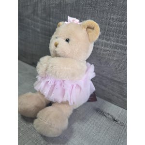 Pu&ograve; includere: Un orsacchiotto di peluche seduto, con un tut&ugrave; rosa chiaro e un fiocco abbinato. L'orso ha la pelliccia marrone chiaro, il naso marrone e gli occhi neri. Il tut&ugrave; &egrave; fatto di tessuto trasparente e scintillante. Un regalo affascinante.
