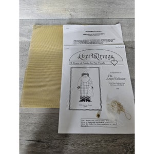 May include: A white and black needlepoint pattern for a Santa Claus design. The pattern is titled "HeartStrings 12 Years of Santa by Pat Thode" and includes the text "2999 Into the Woods Santa".