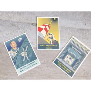 May include: Three vintage-style space-themed postcards. One features an astronaut and a spacecraft with the text "APOLLO & ARTEMIS ROAD TO THE MOON." Another shows a rocket and the text "SIMULATING SPACE EARTH." The third depicts a test facility with the text "SUPER-POWERFUL TEST FACILITIES."