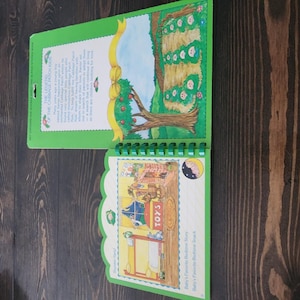 Puede incluir: Un libro de cuentos de Cabbage Patch Kids con encuadernación en espiral y cubierta verde brillante. La página superior presenta un gráfico de cinta amarilla y el texto The Legend of the Cabbage Patch Kids. La inferior muestra una ilustración.