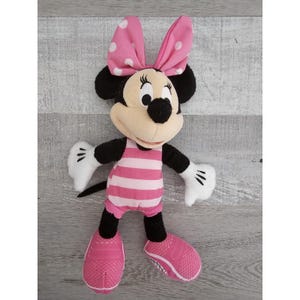 May include: Pink and white striped swimsuit plush toy of Minnie Mouse. She has a pink bow with white polka dots and black shoes.