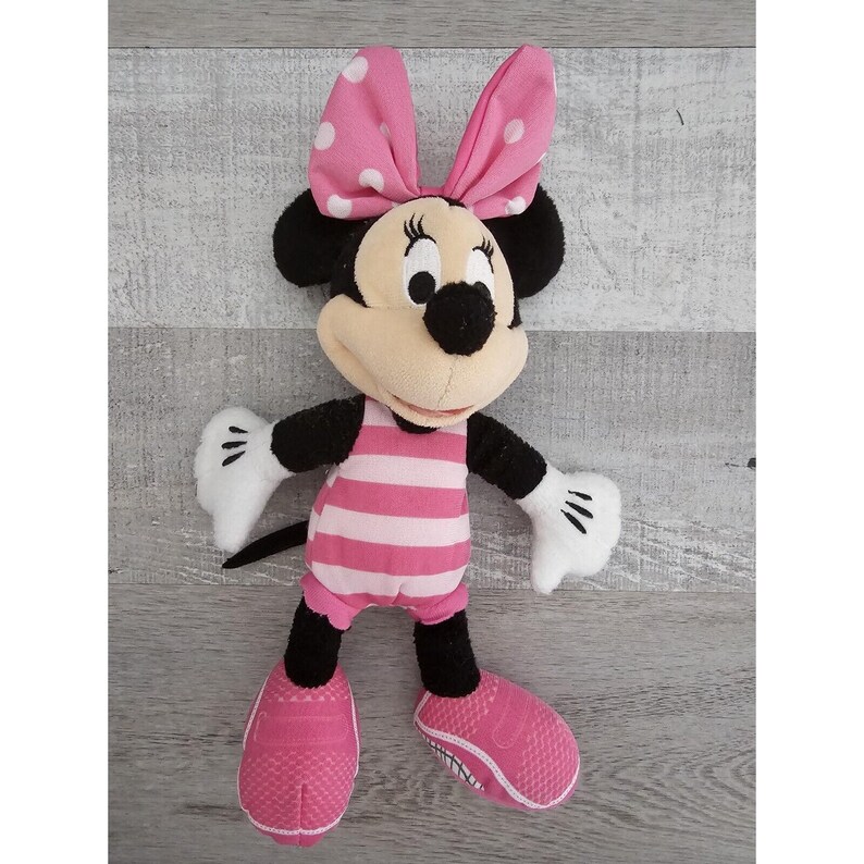 May include: Pink and white striped swimsuit plush toy of Minnie Mouse. She has a pink bow with white polka dots and black shoes.