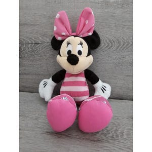 May include: Pink and black plush Minnie Mouse toy with a pink and white striped dress and a pink bow with white polka dots.