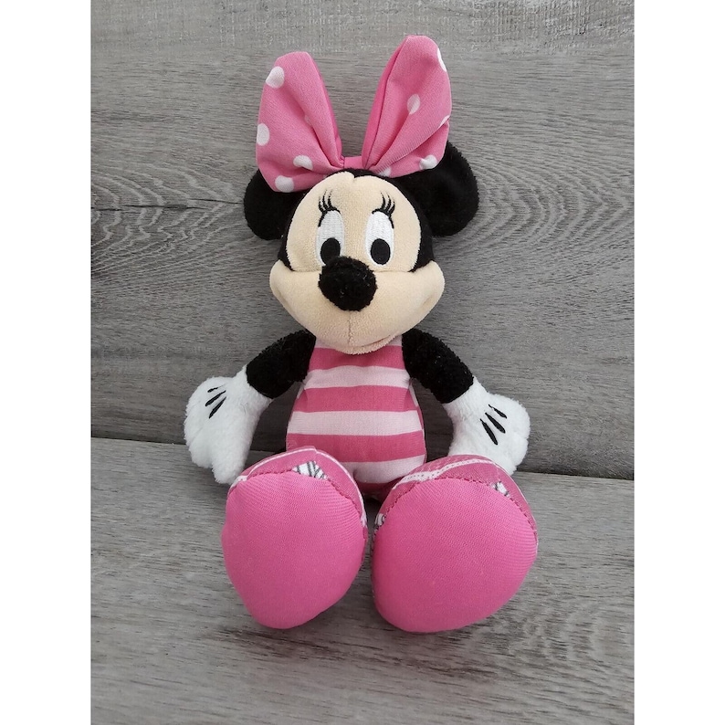 May include: Pink and black plush Minnie Mouse toy with a pink and white striped dress and a pink bow with white polka dots.