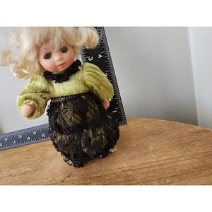 May include: A porcelain doll with blonde hair, wearing a green velvet dress with a black lace skirt.