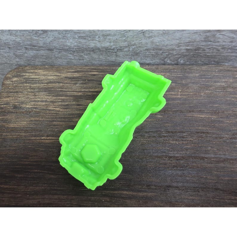 以下が含まれることがあります： 明るい緑色のプラスチック製車型クッキーカッター。カッターは詳細なインテリアデザインと底部の六角形を特徴としています。カッターは木製の表面にあります。