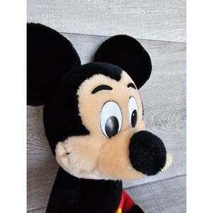 May include: A plush black and tan Mickey Mouse toy with large black ears and white eyes. The toy is looking to the right.