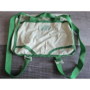 May include: A green and white striped canvas bag with two adjustable straps. The bag has a white label with black text.
