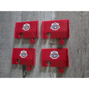 May include: Four red plastic puzzle pieces with the Paw Patrol logo. Each piece has a unique shape with a tab at the bottom and a puzzle piece cutout at the top. The Paw Patrol logo is a blue and white emblem.