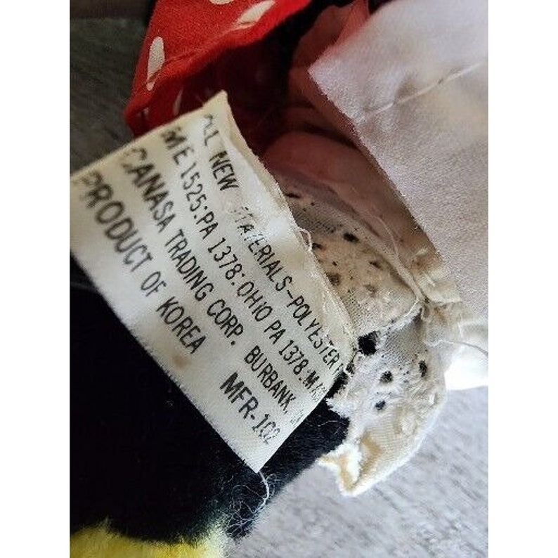 Peut inclure: Gros plan sur un animal en peluche noir et jaune avec un n&oelig;ud rouge &agrave; pois blancs. L'&eacute;tiquette indique "AL NEW MATERIALS-POLYESTER ME 1525:PA 1378: OHIO PA 1378:MA CANASA TRADING CORP. BURBANK. PRODUCT OF KOREA MFR-102".