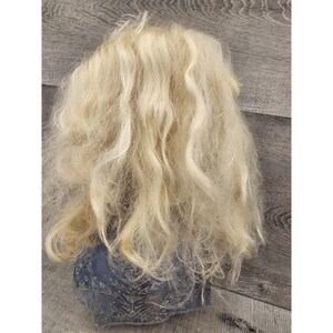 May include: A doll with long, blonde, wavy hair. The doll is wearing a blue and silver dress.