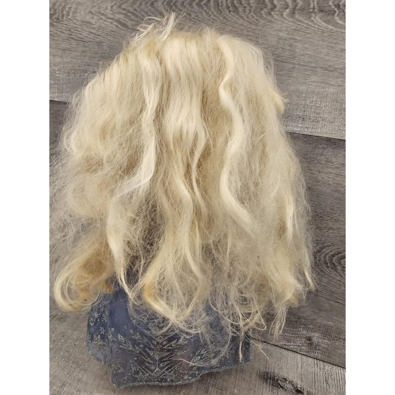 May include: A doll with long, blonde, wavy hair. The doll is wearing a blue and silver dress.