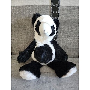 May include: A black and white plush panda bear toy. The panda has a black face and black patches around its eyes. The panda is sitting on a grey surface.