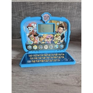 Puede incluir: Un ordenador portátil de juguete azul con personajes de Paw Patrol. El portátil tiene una pequeña pantalla, un teclado e imágenes de perros de dibujos animados. El teclado tiene letras y símbolos. El portátil está abierto y listo para jugar.