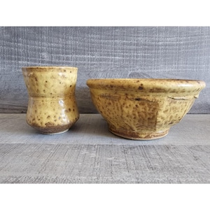 May include: A set of two ceramic bowls in a yellow and brown speckled glaze. The larger bowl is wider and shallower than the smaller bowl.
