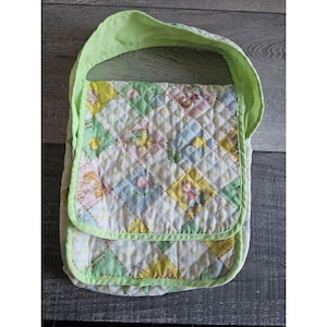 Op de afbeelding: Een groene gewatteerde stoffen tas met een geel en wit ruitpatroon en een print van kinderen met ballonnen. De tas heeft een groene schouderband en een gele bies.