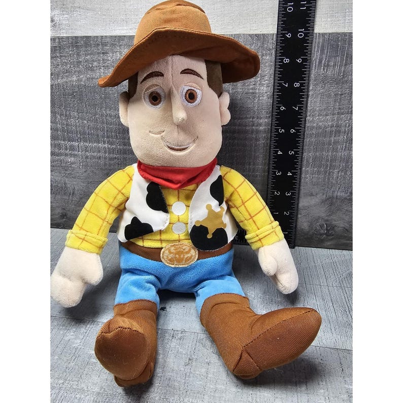 May include: A plush toy of a cartoon cowboy character, featuring a brown hat, a red neckerchief, a yellow plaid shirt, a black and white vest, blue pants, and brown boots. The toy is approximately 10 inches tall.