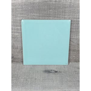 Puede incluir: Un azulejo de cerámica cuadrado con un acabado liso y brillante en un color turquesa claro sólido. El azulejo presenta bordes rectos y limpios con una superficie plana, reflejando la luz de manera uniforme sobre su cara de tono aguamarina.