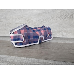 May include: A blue and pink plaid dog coat with a white trim and a small embroidered design.