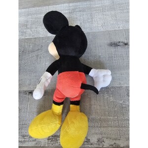 Puede incluir: Un juguete de peluche de Mickey Mouse con orejas negras, cuerpo negro, pantalones cortos rojos y zapatos amarillos.