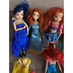 Op de afbeelding: Een verzameling modepoppen met levendig haar en gedetailleerde outfits. De poppen hebben verschillende kleuren, waaronder blauw, rood en geel. De poppen zijn gekleed in jurken en rokken, met accessoires zoals laarzen en gouden randen.