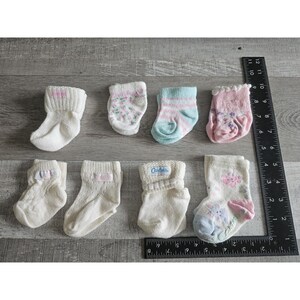 Puede incluir: Una colecci&oacute;n de ocho pares de calcetines para beb&eacute; en varios colores y patrones, incluyendo dise&ntilde;os blancos, rosas, azules y florales. Algunos calcetines tienen la palabra "Cartoks" impresa en ellos.